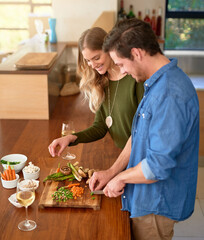 Wall Mural - Making the perfect meal together. Shot of a smiling young couple standing at their kitchen counter chopping up ingredients together for dinner.