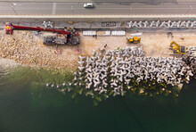 Aerial View Of Breakwater Construction. Bulldozer And Crane On A Pile Of Boulders In The Sea