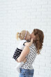 © satura_ - Mother holds her child with hearing aids and cochlear implants on white brick wall . Deaf and health concept