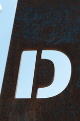 the letter D hewn from sheet of rusty metal and sky