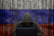 The troll factory. A hacker is sitting at a laptop and against the background of the Russian flag, attacking and hacking corporate servers with a virus. Concept: DDOS attack, fake news.