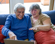 Elderly couple making a remote video call with grandchildren, retirees using a laptop and internet connections for shopping, grandparents watching something fun on the web
