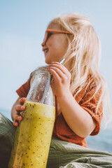 Wall Mural - Child girl drinking kiwi smoothie with glass bottle baby vegan food healthy lifestyle summer family vacations detox beverage