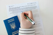 Woman hand write with a pen in PESEL document on white table. Ukrainian passport on white background.