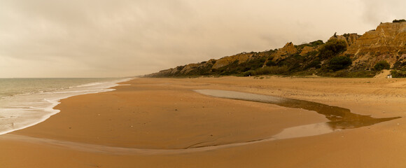 Poster - panorama view of a beautiful long and empty beach with shore break and high sand dunes behind and sahara dust in the air