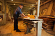 © bondvit - Senior carpenter in uniform works on a woodworking machine at the carpentry manufacturing