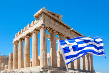 World Famous Iconic Parthenon On The Acropolis Hill In Athens, Greece With Greek Flag Against Blue Sky
