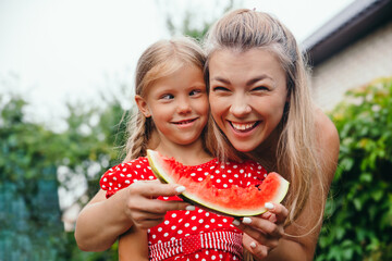 happy mother and daughter eating watermelon and having fun outdoor in summer day