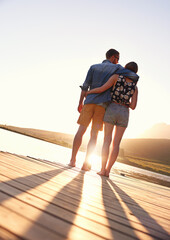 Wall Mural - The end to a perfect day together. Rearview shot of an affectionate young couple standing on a dock at sunset.