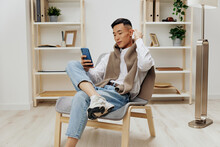 Teenager Sitting In A Chair In A Room With Phone On His Lap