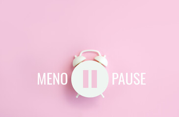 word menopause, pause sign on a white alarm clock on pink background. minimal concept hormone replac