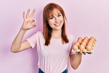 Sticker - Redhead young woman showing fresh eggs doing ok sign with fingers, smiling friendly gesturing excellent symbol