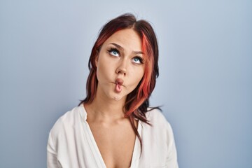 Wall Mural - Young caucasian woman wearing casual white shirt over isolated background making fish face with lips, crazy and comical gesture. funny expression.