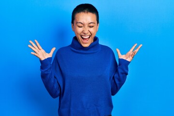 Wall Mural - Beautiful hispanic woman with short hair wearing turtleneck sweater celebrating mad and crazy for success with arms raised and closed eyes screaming excited. winner concept