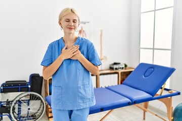 Canvas Print - Beautiful caucasian physiotherapist woman working at pain recovery clinic smiling with hands on chest with closed eyes and grateful gesture on face. health concept.