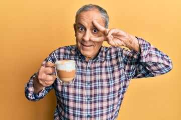 Wall Mural - Handsome senior man with grey hair drinking a cup coffee doing peace symbol with fingers over face, smiling cheerful showing victory