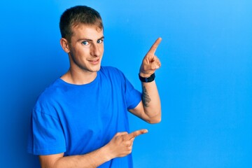 Poster - Young caucasian man wearing casual blue t shirt smiling and looking at the camera pointing with two hands and fingers to the side.