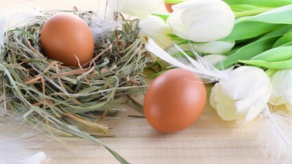 Wall Mural - Easter eggs color in basket with spring tulips, white feathers on wooden table background in Happy Easter decoration. Festive decoration