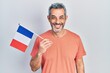 Handsome middle age man with grey hair holding france flag looking positive and happy standing and smiling with a confident smile showing teeth