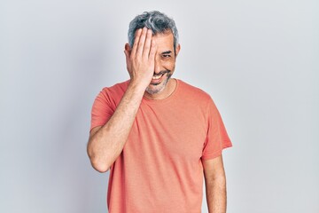 Poster - Handsome middle age man with grey hair wearing casual t shirt covering one eye with hand, confident smile on face and surprise emotion.