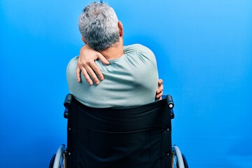 Poster - Handsome middle age man with grey hair sitting on wheelchair hugging oneself happy and positive from backwards. self love and self care