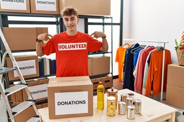 Wall Mural - Young caucasian man volunteer holding donations box looking confident with smile on face, pointing oneself with fingers proud and happy.