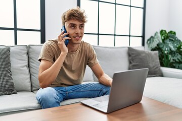 Sticker - Young caucasian man using laptop talking on the smartphone at home