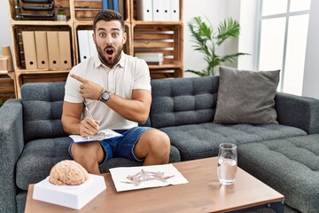 Canvas Print - Handsome hispanic man working with rorschach test at psychology clinic surprised pointing with finger to the side, open mouth amazed expression.