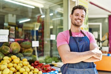 Poster - Young hispanic worker wearing apron standing with arms crossed gesture at the fruit store.