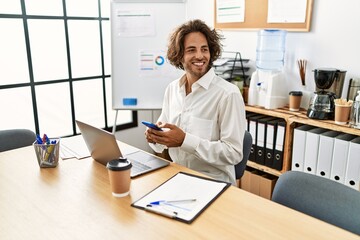 Wall Mural - Young hispanic businessman smiling happy using smartphone at office.