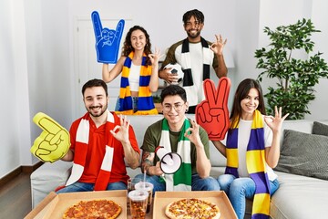 Canvas Print - Group of young people wearing team scarf cheering football game doing ok sign with fingers, smiling friendly gesturing excellent symbol