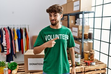 Poster - Young arab man wearing volunteer t shirt at donations stand pointing with hand finger to the side showing advertisement, serious and calm face