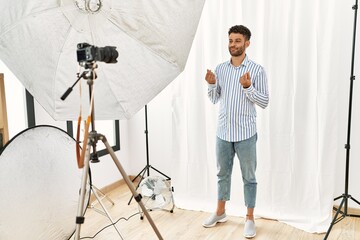 Sticker - Arab young man posing as model at photography studio doing money gesture with hands, asking for salary payment, millionaire business