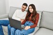 © Krakenimages.com - Young hispanic couple using laptop sitting on the sofa at home.