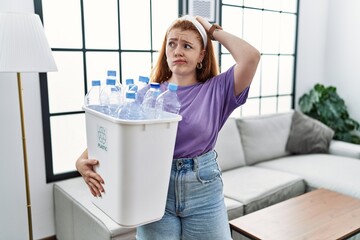 Sticker - Young redhead woman holding recycling wastebasket with plastic bottles confuse and wondering about question. uncertain with doubt, thinking with hand on head. pensive concept.