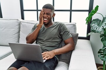 Wall Mural - Young african american man using laptop at home sitting on the sofa yawning tired covering half face, eye and mouth with hand. face hurts in pain.