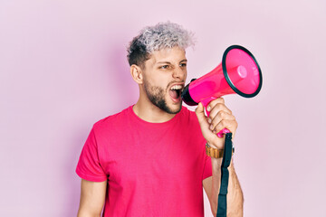 Wall Mural - Young hispanic man screaming with megaphone over pink background