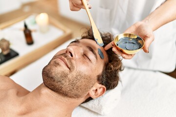 Poster - Young hispanic man having facial mask treatment at beauty center