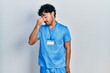 © Krakenimages.com - Young hispanic man wearing blue male nurse uniform tired rubbing nose and eyes feeling fatigue and headache. stress and frustration concept.