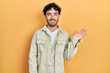 Poster - Young hispanic man wearing casual clothes smiling cheerful presenting and pointing with palm of hand looking at the camera.