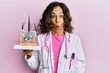 Middle age hispanic doctor woman holding model of human anatomical skin and hair scared and amazed with open mouth for surprise, disbelief face