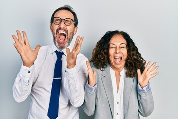 Middle age couple of hispanic woman and man wearing business office uniform celebrating mad and crazy for success with arms raised and closed eyes screaming excited. winner concept