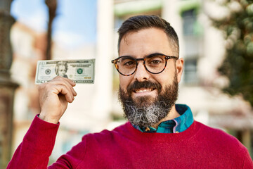 Young hispanic executive man smiling happy holding 20 dollars banknote at the city.