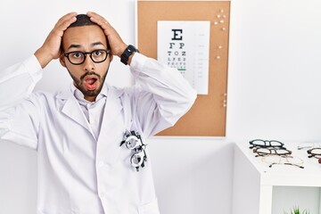 Poster - African american optician man standing by eyesight test crazy and scared with hands on head, afraid and surprised of shock with open mouth