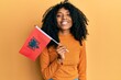 © Krakenimages.com - African american woman with afro hair holding albania flag looking positive and happy standing and smiling with a confident smile showing teeth
