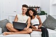 © Krakenimages.com - Young interracial couple using laptop at home sitting on the sofa with a happy and cool smile on face. lucky person.