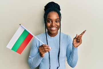 Poster - African american woman with braided hair holding bulgaria flag smiling happy pointing with hand and finger to the side