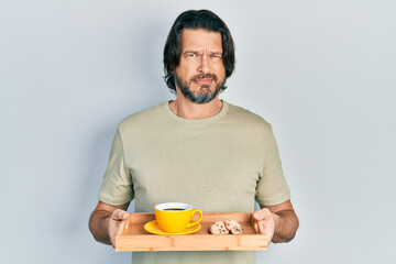 Canvas Print - Middle age caucasian man holding breakfast tray with cookies and coffee skeptic and nervous, frowning upset because of problem. negative person.