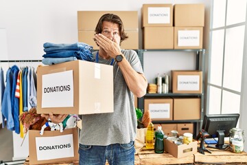 Canvas Print - Handsome middle age man holding donations box for charity at volunteer stand shocked covering mouth with hands for mistake. secret concept.