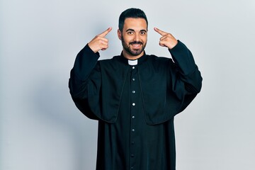 Sticker - Handsome hispanic man with beard wearing catholic priest robe smiling pointing to head with both hands finger, great idea or thought, good memory